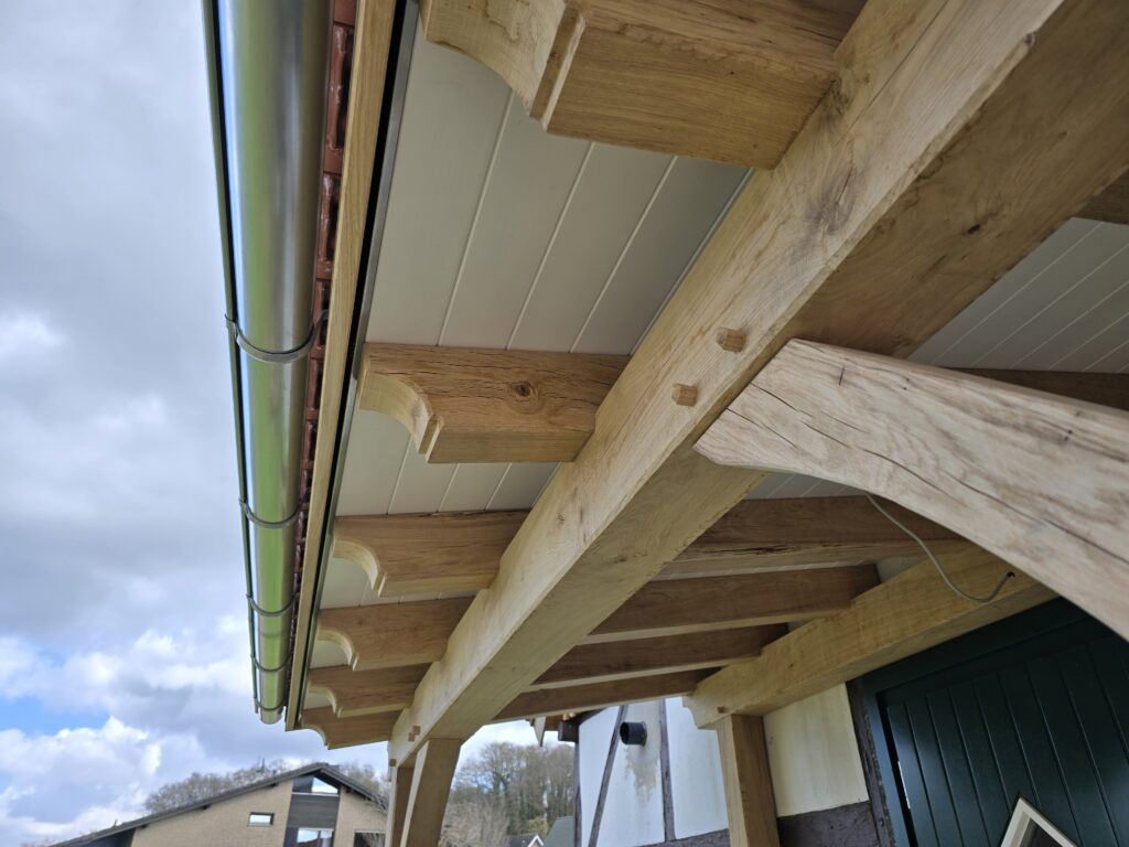 Holzkonstruktion mit Dachrinne an einem Gebäude; weiße und grüne Fassade, bewölkter Himmel.
