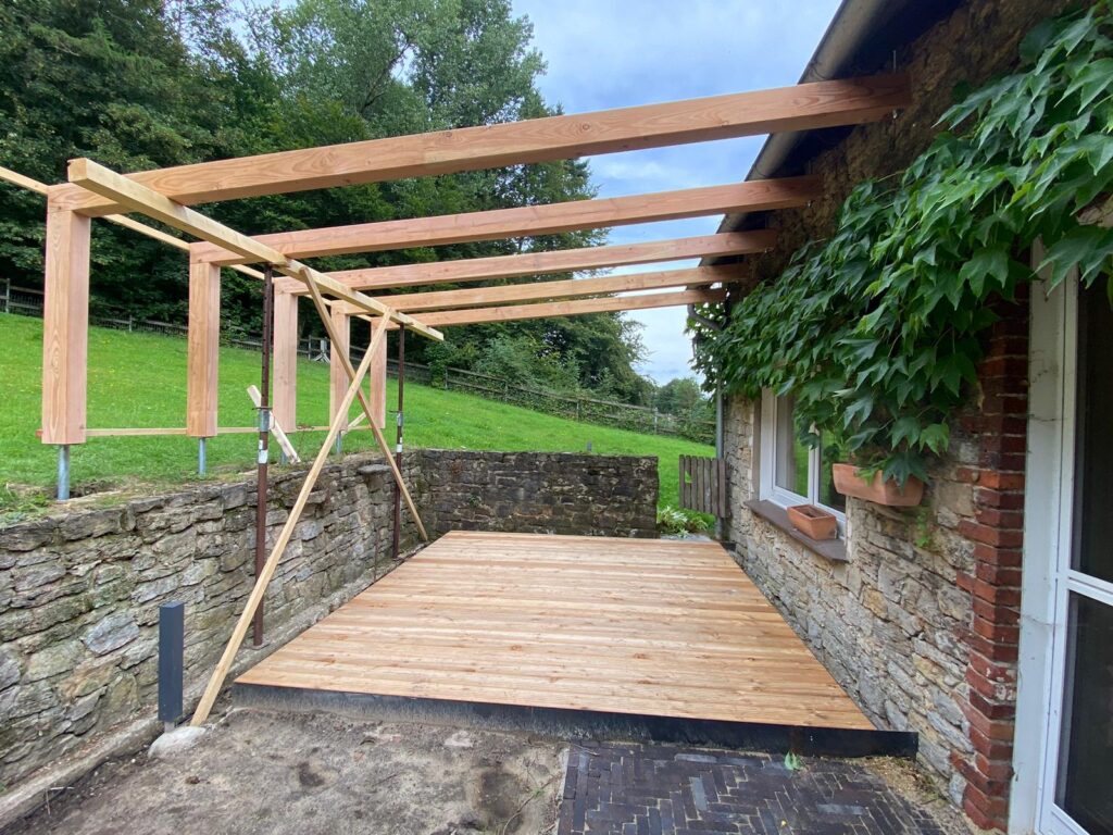 Teilweise überdachte Terrasse im Bau mit Holzstruktur, Steinmauer und grüner Pflanzenwand.