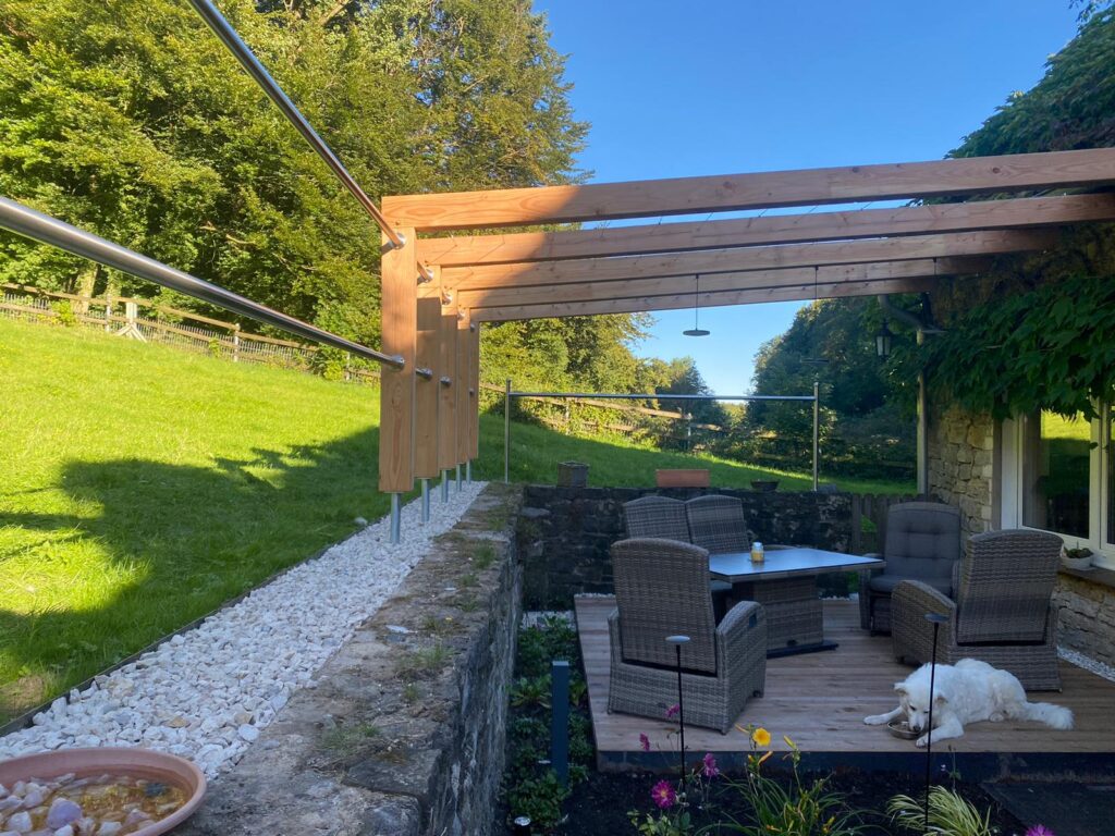 Gemütliche Terrasse mit Rattanmöbeln, umgeben von Natur; ein weißer Hund ruht entspannt darauf.