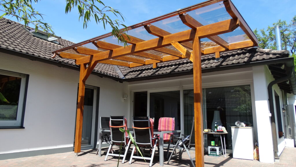 Eine sonnige Terrasse mit Holzpergola, Tisch und Stühlen, ideal für entspannte Freizeit im Freien.