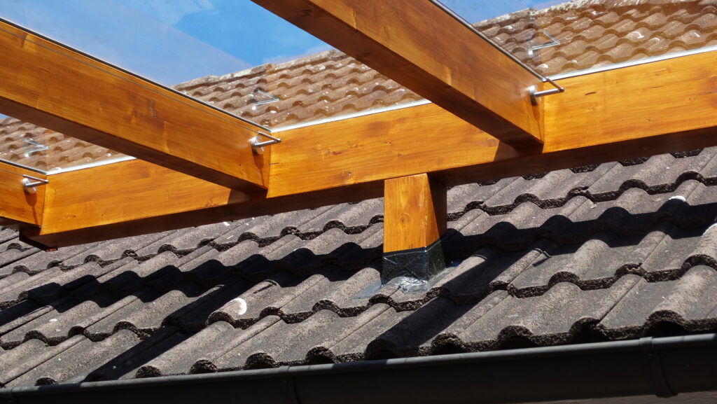 Holz-Glas-Überdachung über einem dunklen Ziegeldach, blauer Himmel im Hintergrund.