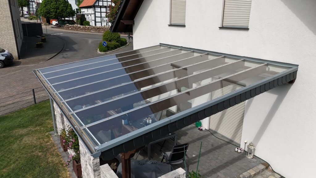 Überdachte Terrasse mit Gartenmöbeln, umgeben von Pflanzen, in einer ruhigen Wohngegend.