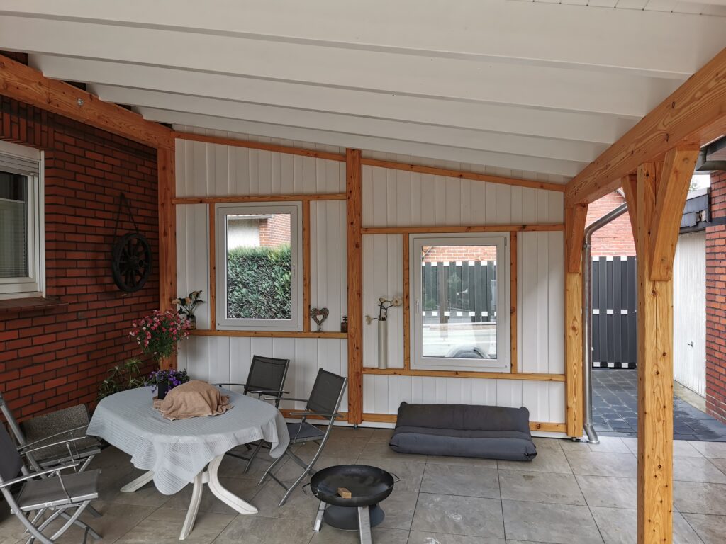 Überdachte Terrasse mit Tisch, Gartenstühlen, Grill und Blumenarrangements, ruhig und einladend.