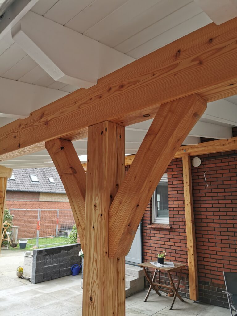 Überdachte Terrasse mit Holzbalken, Ziegelwand, kleinem Tisch und Pflanze, einladend und rustikal.