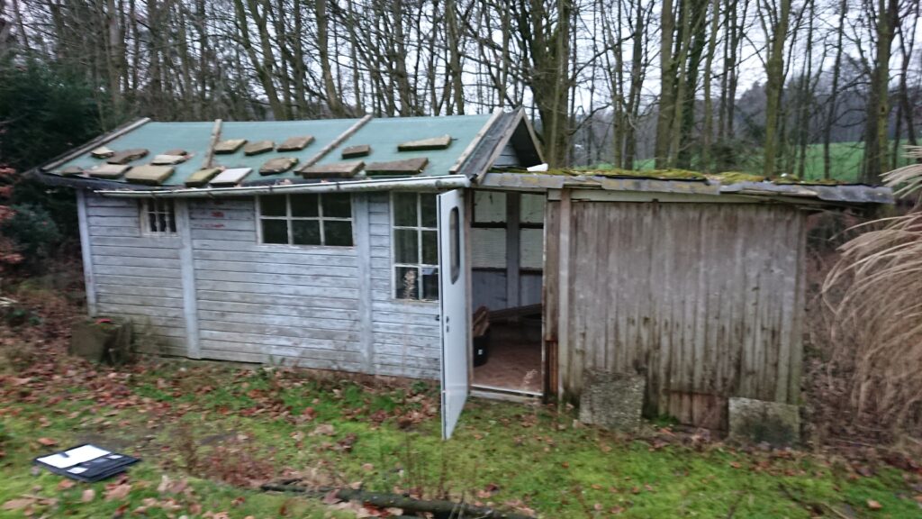 Verlassene, verwitterte Hütte im Wald mit offenstehender Tür und moosbewachsenem Dach.