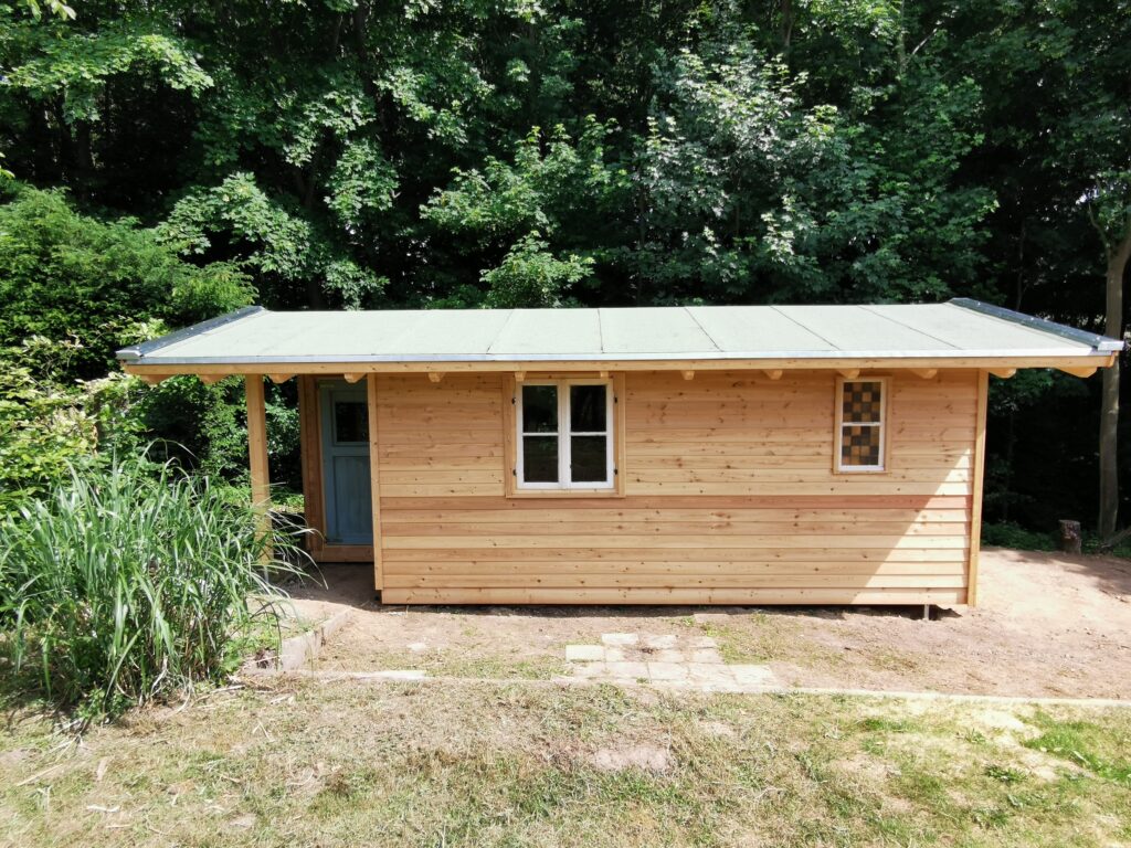 Kleine Holzhütte mit grünem Dach, umgeben von üppigem Laub, vermittelt Ruhe und Einfachheit.