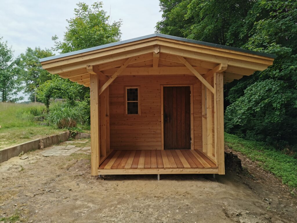 Eine kleine Holzhütte steht friedlich in einer grünen, natürlichen Umgebung mit Bäumen und Pflanzen.