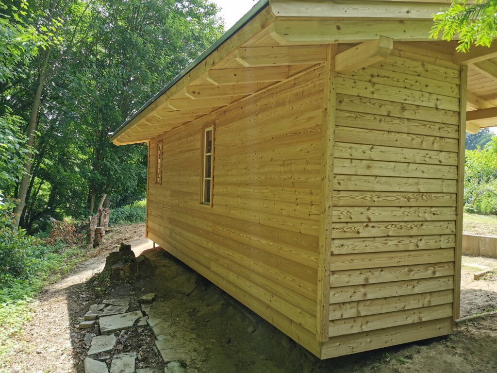 Eine Holzhütte im Wald mit einem Steinpfad, umgeben von üppigem Grün und Sonnenlicht.