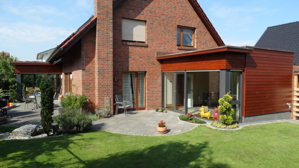Modernes Einfamilienhaus aus roten Ziegeln mit gepflegtem Garten und Terrasse bei sonnigem Wetter.