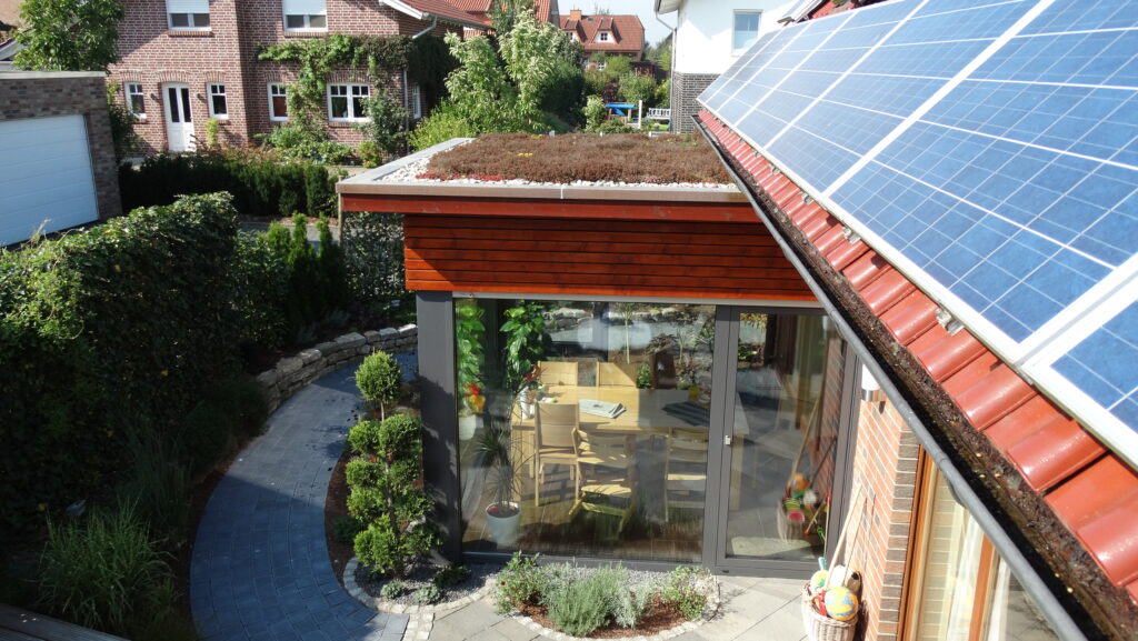 Moderne Wohnsiedlung mit begrüntem Dach, Solarpaneelen und Gartenweg, betont Nachhaltigkeit.