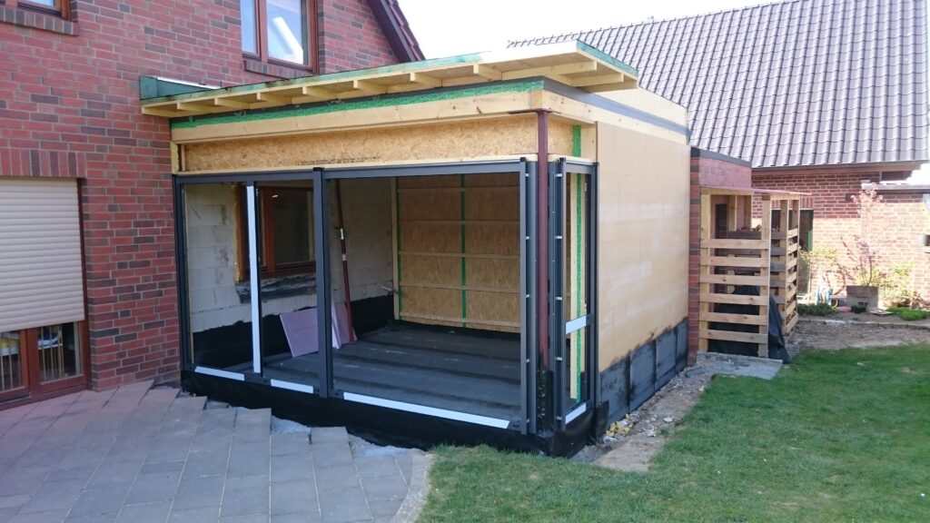 Eine Baustelle mit einem Anbau aus Holz und Metall, der an ein rotes Backsteinhaus anschließt.