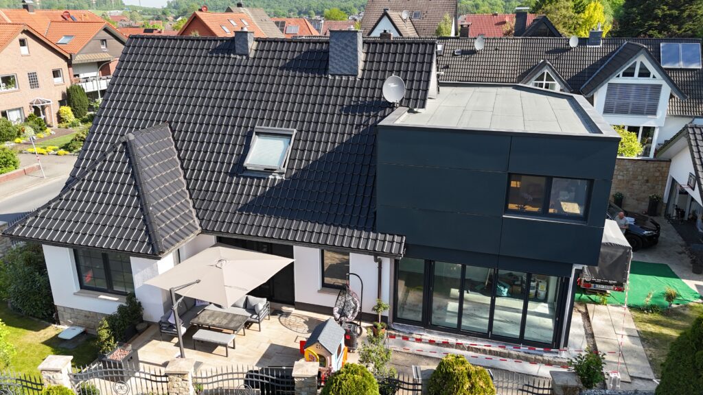 Modernes Wohnhaus mit traditionellem Dach, Terrasse, Spielbereich und geparktem Auto in ruhiger Umgebung.