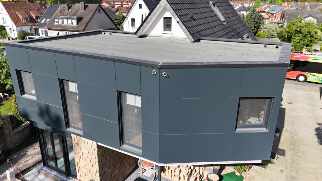 Modernes Gebäude mit dunkler Fassade, großen Fenstern und Bauutensilien, umgeben von traditionellen Häusern.