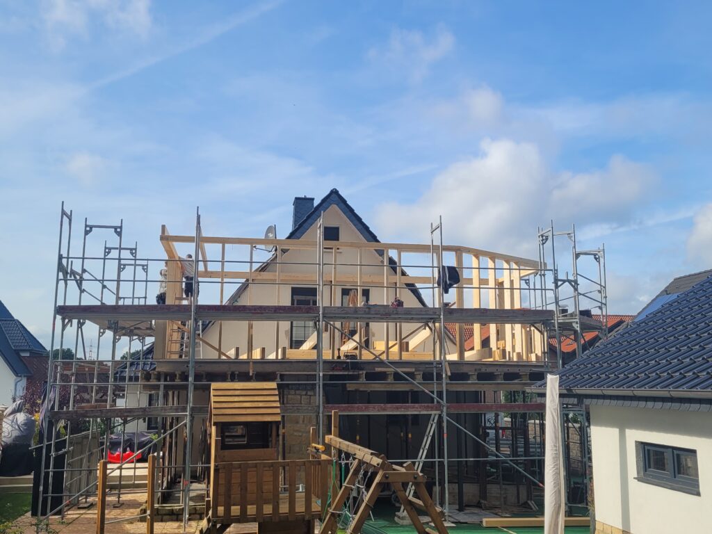 Ein zweistöckiges Haus wird mit einem Gerüst renoviert, während ein Spielhaus im Vordergrund steht.