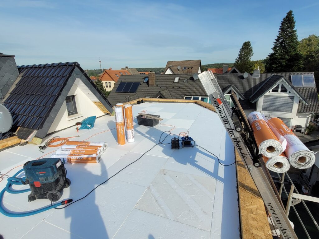 Baustelle auf einem Flachdach mit Solarpaneelen, Materialien und Werkzeugen bei sonnigem Wetter.