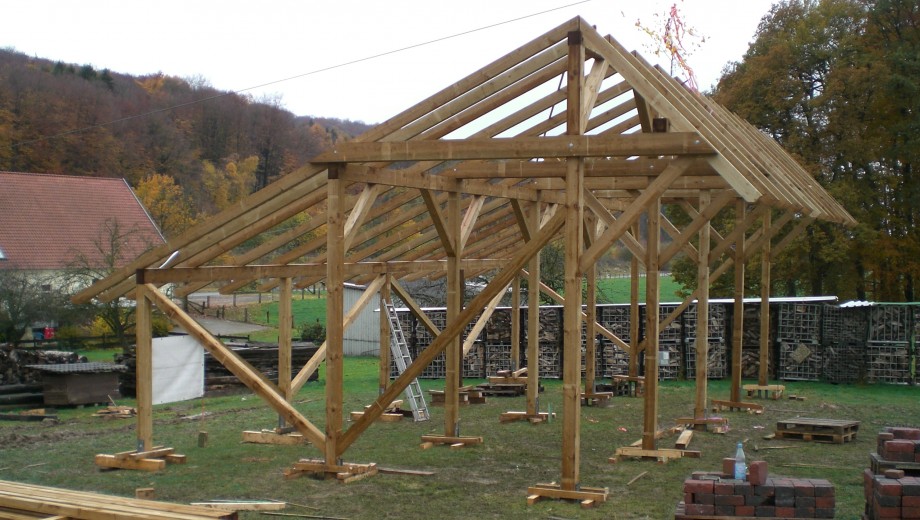 Holzrahmenbau einer Scheune im ländlichen Umfeld, umgeben von Herbstbäumen und Bauutensilien.