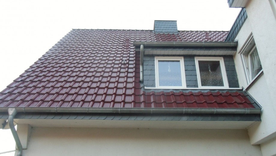 Ein gepflegtes Hausdach mit roten Ziegeln, weißen Fensterrahmen und grauen Schieferplatten um die Fenster.