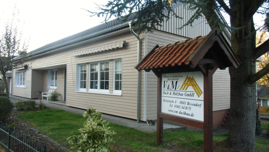 Ein modernes Gebäude mit Holzfassade, großen Fenstern und einem Firmenschild für Dach- und Holzbau.