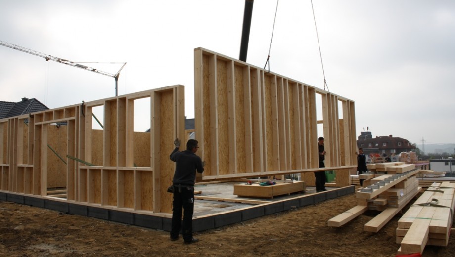 Eine Baustelle mit Arbeitern, die einen großen Holzrahmen mithilfe eines Krans positionieren.