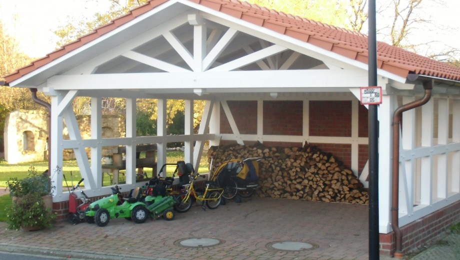 Überdachter Unterstand mit Holzstapeln, Kinderspielzeug und Fahrrädern; ländliche, familiäre Umgebung.