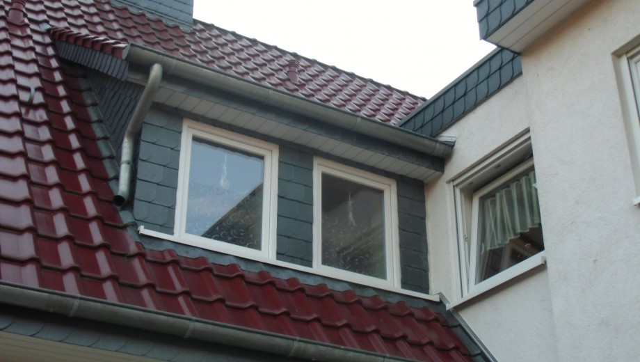 Ein Gebäude mit roten Ziegeldach, weißen Fenstern und grauer Schiefer- sowie weißer Putzfassade.