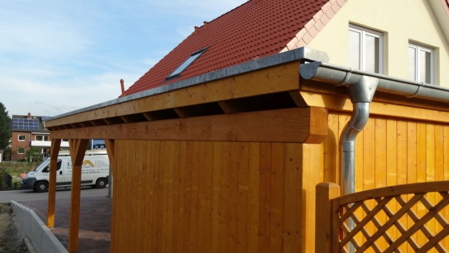 Holzüberdachung an Haus mit rotem Ziegeldach, silberner Regenrinne und blauem Himmel im Hintergrund.