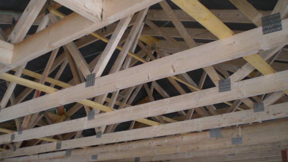 Holzdachkonstruktion mit Fachwerkstil, verbunden durch metallische Elemente, zeigt Stabilität und Präzision.