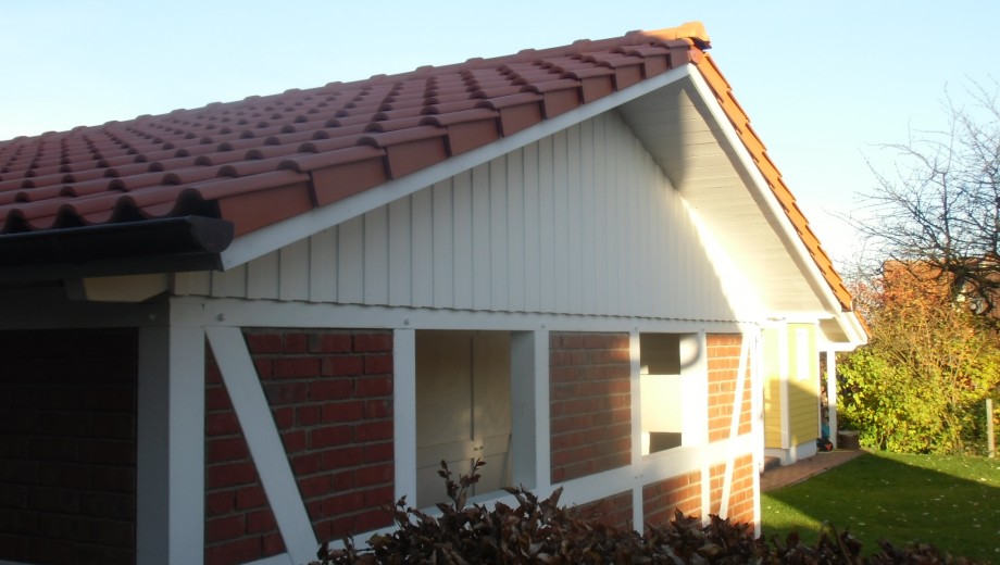 Ein Haus mit roten Dachziegeln und Fachwerkfassade, umgeben von Pflanzen, bei sonnigem Wetter.