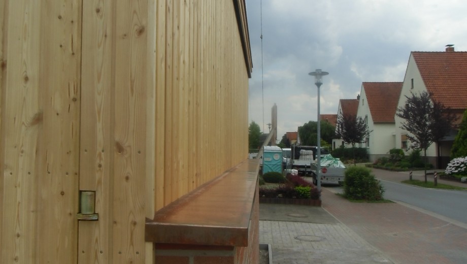 Ruhige Wohnstraße mit Holzfassade, geparktem Transporter und Einfamilienhäusern unter grauem Himmel.