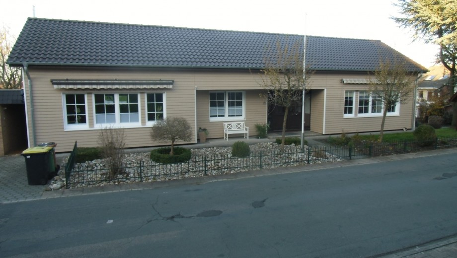 Modernes einstöckiges Haus mit Holzfassade, großem Fenster, gepflegtem Vorgarten und kleinem Zaun.