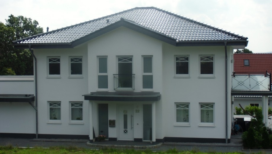 Modernes, zweistöckiges Einfamilienhaus mit weißer Fassade und dunkelgrauem Dach an einem bewölkten Tag.