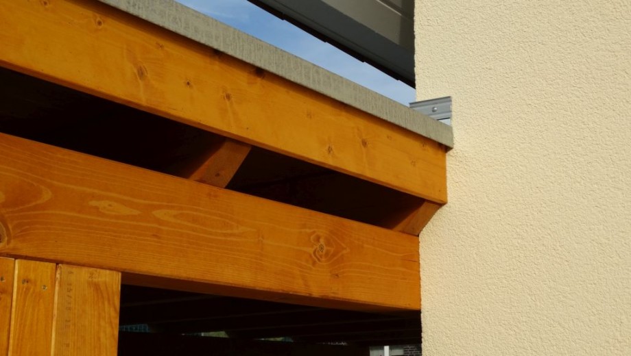 Holzbalken und verputzte Wand in warmen Tönen, mit sichtbarer Holzmaserung und blauem Himmel.