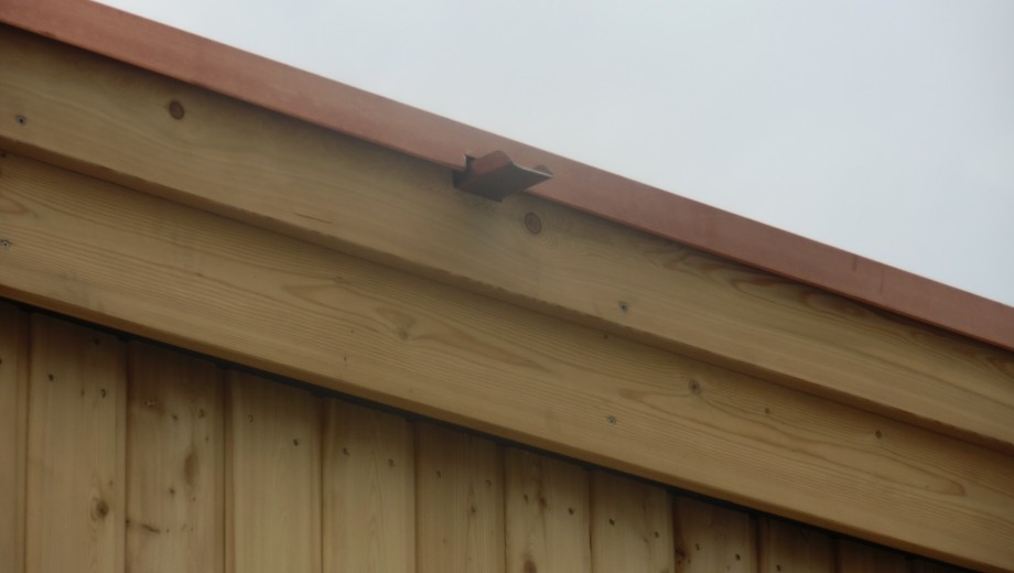 Ein Dach mit rötlich-braunem Rand und hellem Holzüberhang vor bewölktem Himmel, rustikale Atmosphäre.