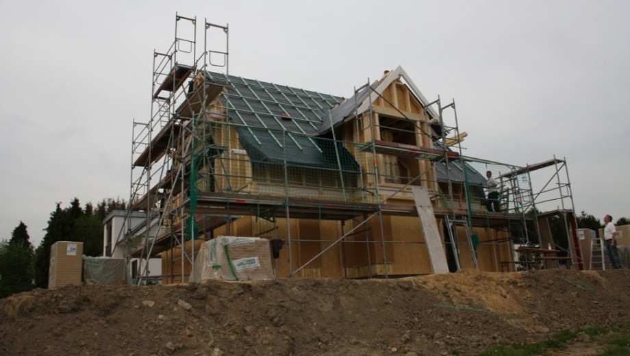 Eine Baustelle mit Bauarbeitern auf einem Gerüst, die an einem Einfamilienhaus arbeiten. Bewölkter Himmel.