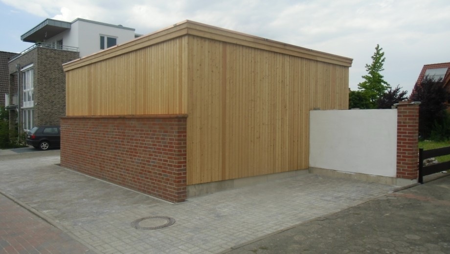 Moderne Garage mit Holz- und Ziegelfassade, umgeben von städtischen Wohnhäusern und gepflasterter Einfahrt.