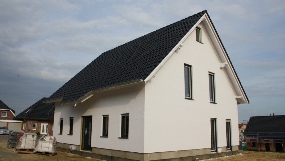 Modernes Einfamilienhaus mit weißer Fassade und dunklem Dach, umgeben von Baumaterialien.