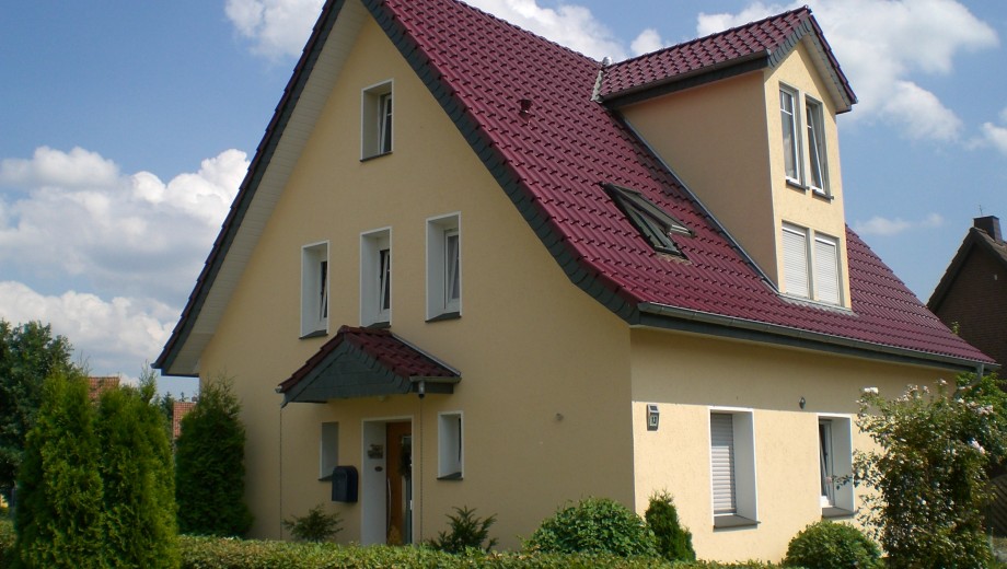 Ein modernes, zweistöckiges Einfamilienhaus mit rotem Dach in einem gepflegten Garten unter blauem Himmel.