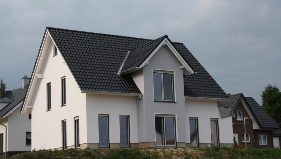 Modernes Einfamilienhaus mit weißer Fassade und dunklem Satteldach vor bewölktem Himmel.