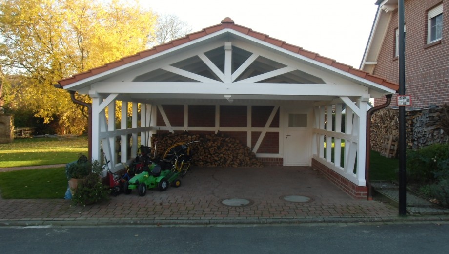 Carport mit rotem Ziegeldach, Holzstapel und Kinderfahrzeugen; Herbstbaum und Haus im Hintergrund.
