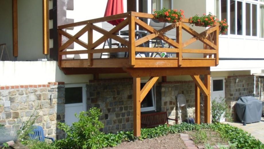 Erhöhte Holzterrasse mit Gartenmöbeln, rotem Sonnenschirm und Blumenkästen, umgeben von Natursteinwand.