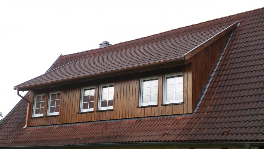 Ein Hausdach mit roten Ziegeln und einer Holzgaube mit vier weißen Fensterrahmen.