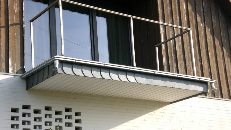 Ein moderner Balkon mit Glasbrüstung und Metallgeländer an einer Holz- und Ziegelfassade.