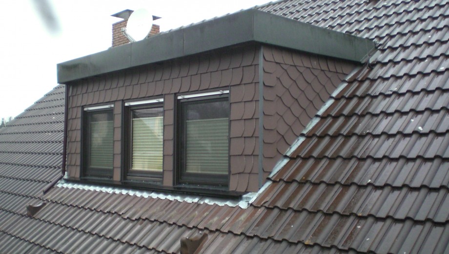 Ein Hausdach mit dunkelbraunen Ziegeln, drei Dachfenstern und einer weißen Satellitenschüssel.