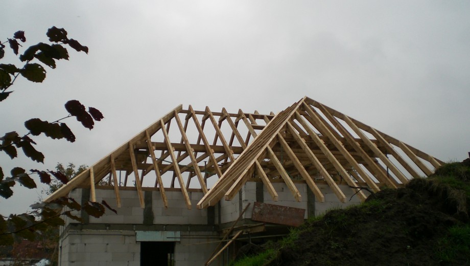 Baustelle mit teilweise errichtetem Dachstuhl aus Holz auf einem Gebäude aus Beton oder Ziegelsteinen.