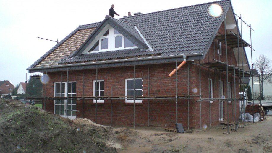 Ein im Bau befindliches Einfamilienhaus mit roter Ziegelfassade und zwei Arbeitern auf dem Dach.