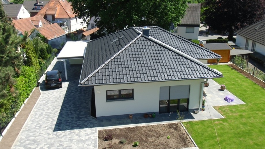 Modernes Einfamilienhaus mit weißer Fassade, dunklem Dach und gepflegtem Garten in ruhiger Nachbarschaft.