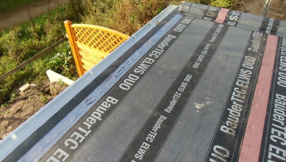 Dach mit BauderTEC ELWS DUO Abdichtungsbahnen, umgeben von grünem Garten und Holzzaun im Hintergrund.