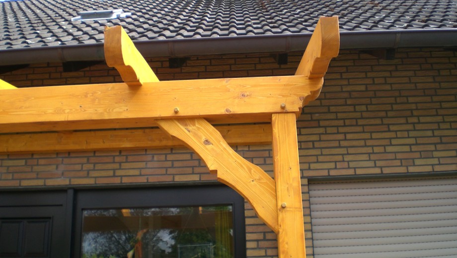 Holzüberbau an gelber Ziegelfassade mit dunklem Ziegeldach, vermittelt Stabilität und Handwerkskunst.
