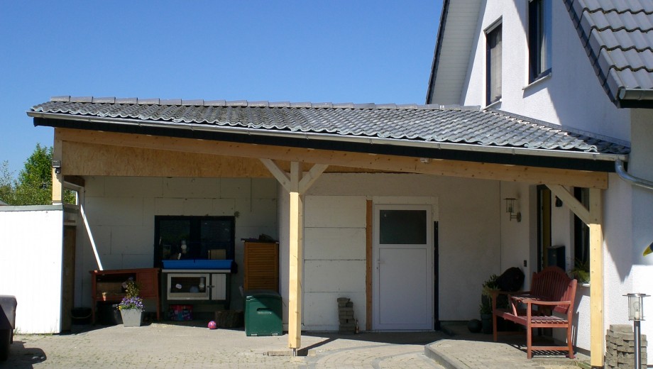 Weißes Haus mit Carport, rotem Stuhl, Kaninchenstall und Blumen; ruhige, sonnige Vorstadtszene.