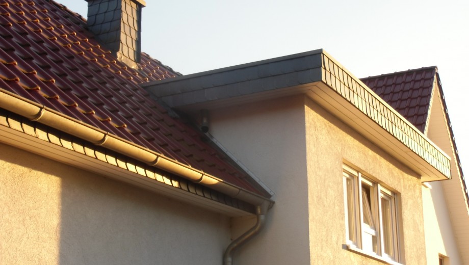 Ein Hausdach mit roten Ziegeln, einem Schornstein und einem Fenster in einer ruhigen Wohngegend.